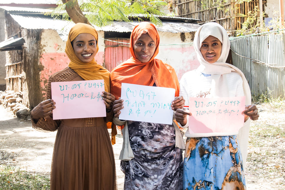 Youth activists Radwa, 18, Samira, 19, and Hayat, 18, hold up signs that read "Stop child trafficking!" "End child marriage!" and "End child labor!" in their native language, Amharic.